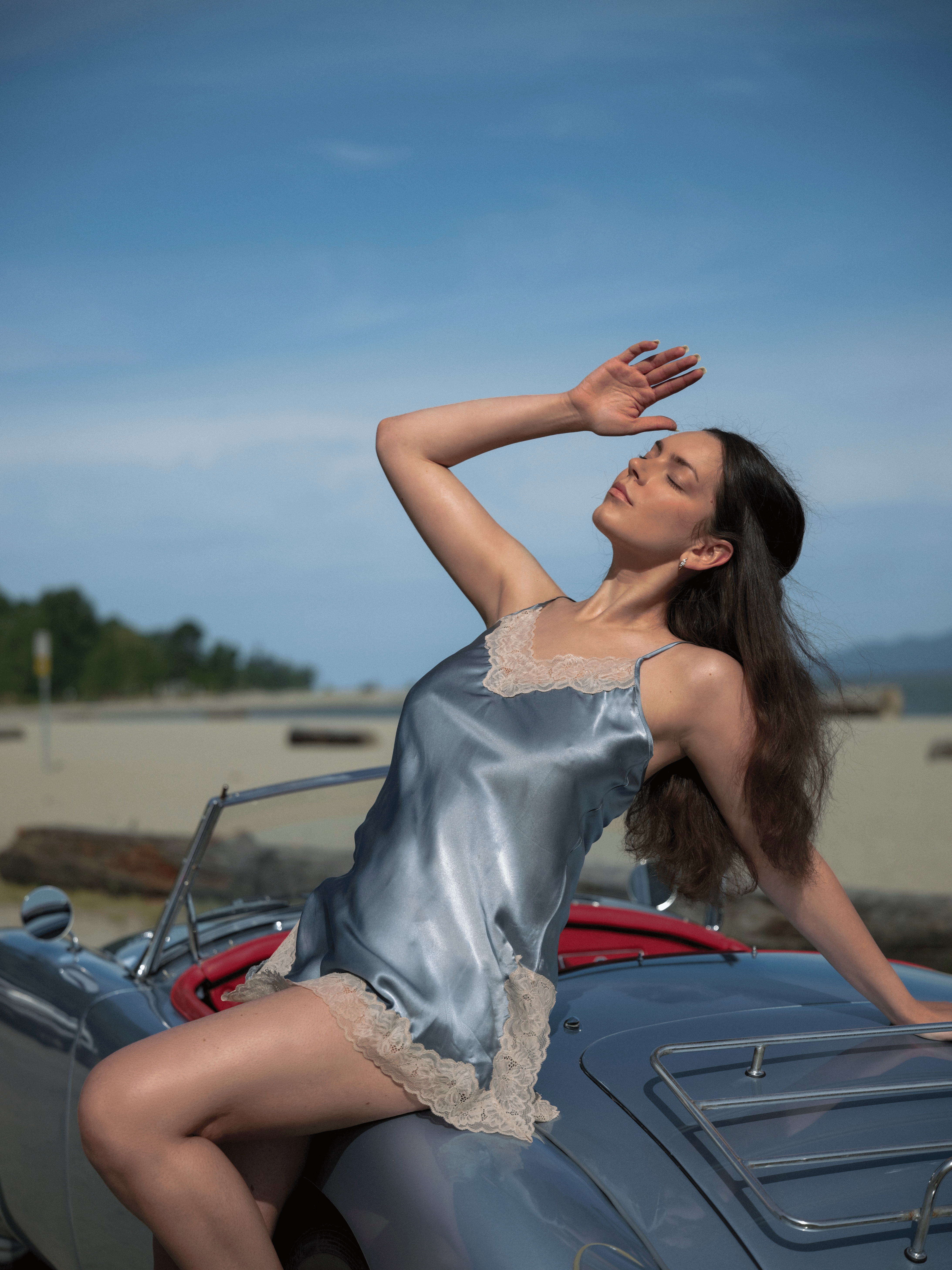 a girl wearing a blue silk dress in a blue car beside the sea